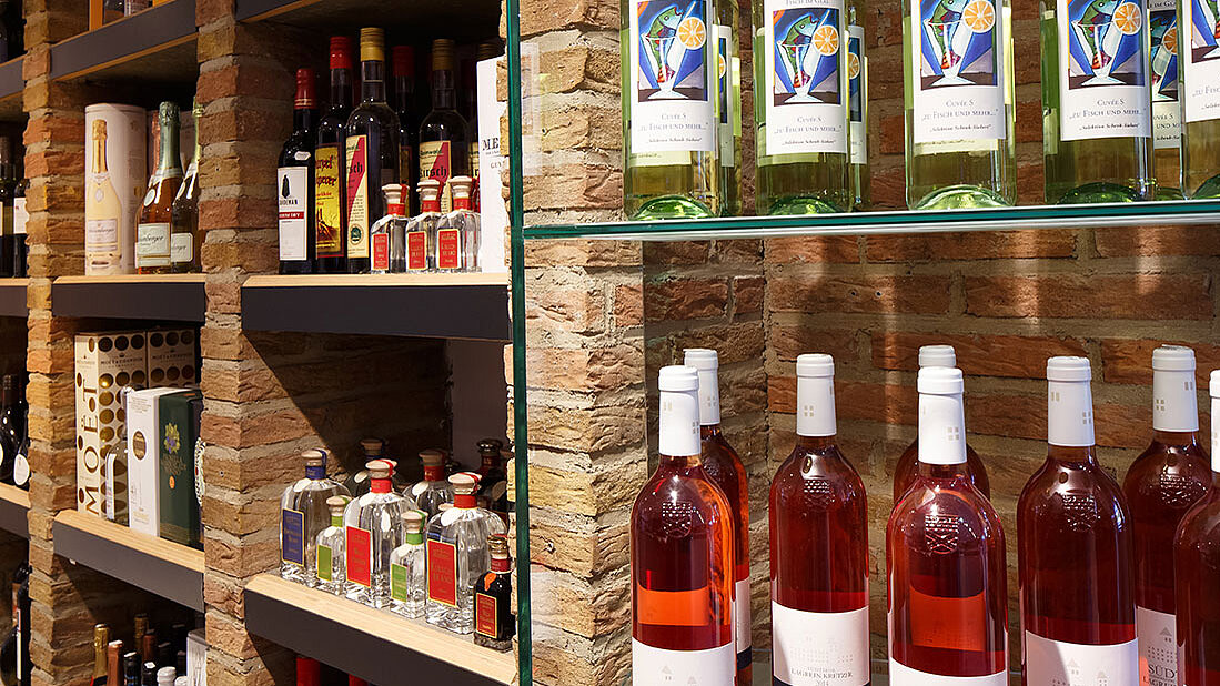 Regale mit Wein-, Likör- & Spirituosenflaschen in einer Feinkostabteilung mit Backsteinwänden & stilvoller Präsentation