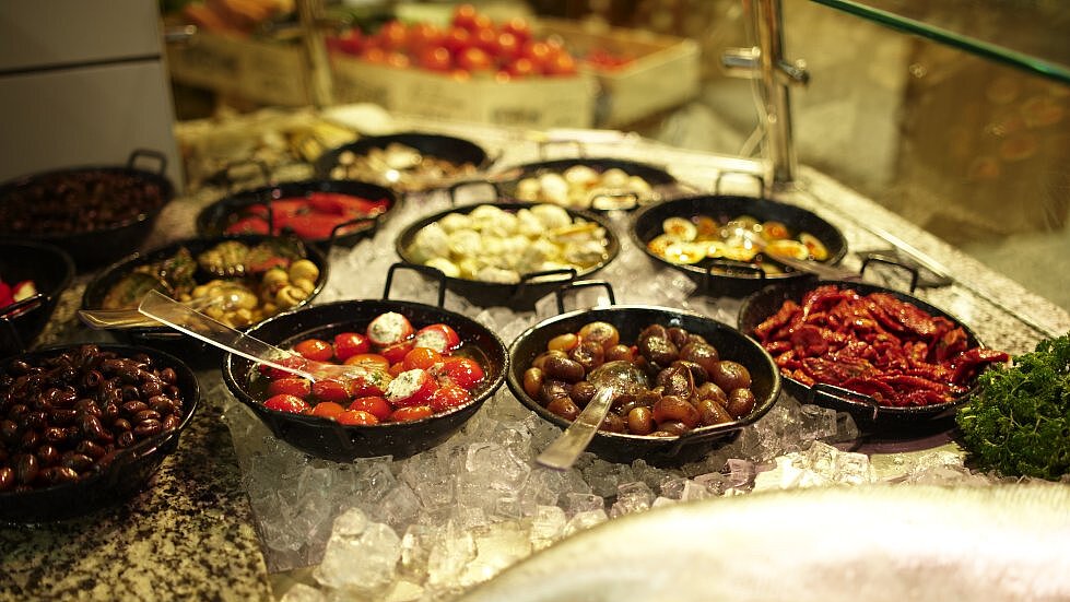 Auswahl an Antipasti wie Oliven, Paprika, Tomaten & gefülltem Gemüse in schwarzen Schalen auf Eis in einer Feinkosttheke